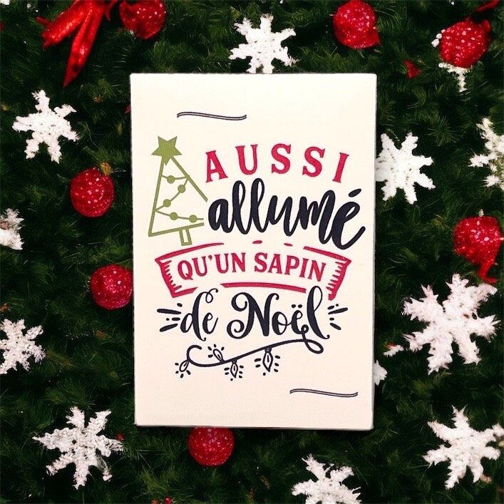 French Christmas seed packet reading 'Aussi allumé qu'un sapin de Noël' lying in a Christmas wreath decorated with white snowflakes and red baubles