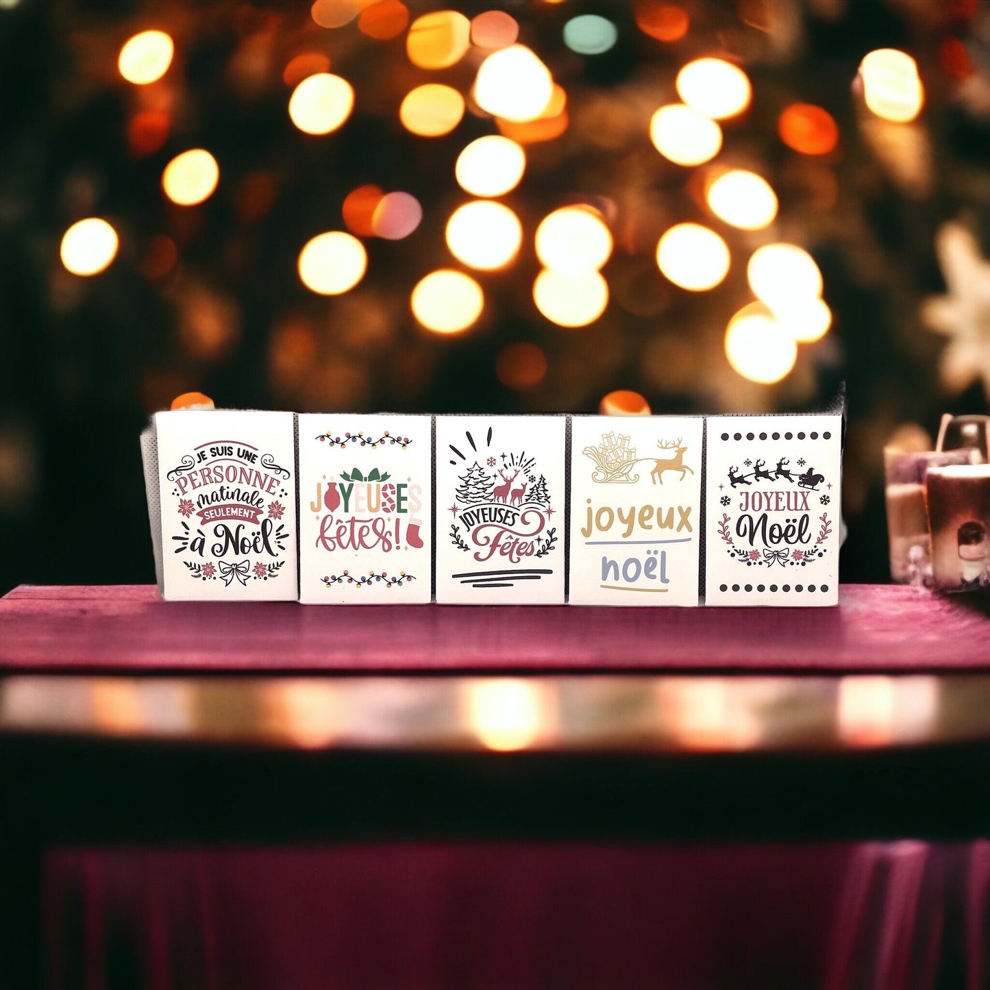 Five French Christmas seed packets in a row in front of Christmas tree lights, reading 'Je suis une personne matinale seulement à Noël', 'Joyeuses fêtes!', 'Joyeuses Fêtes', 'joyeux noël' and 'Joyeux Noël'