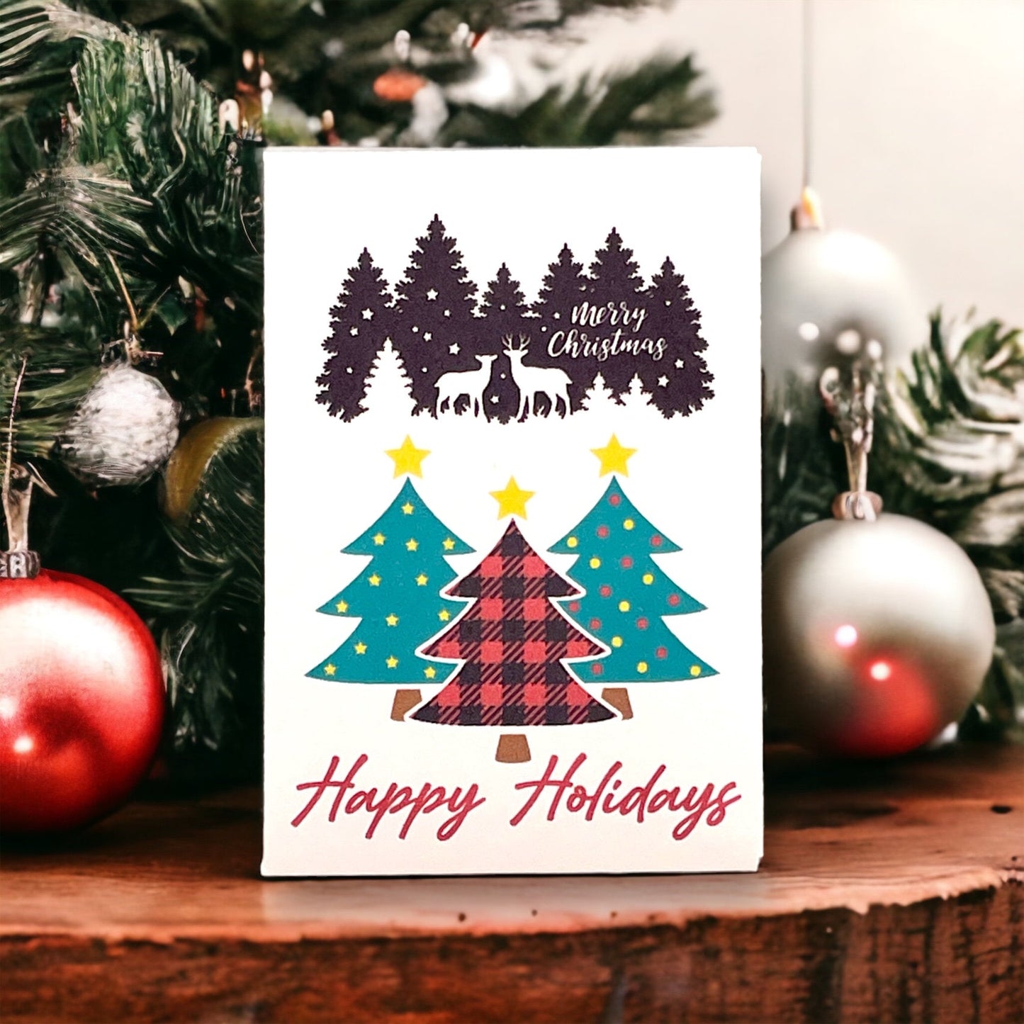 Woodland Christmas seed packet showing two deer in a pine forest with 'Merry Christmas' written in the trees, above three decorated Christmas trees in teal and red plaid and the words 'Happy Holidays'