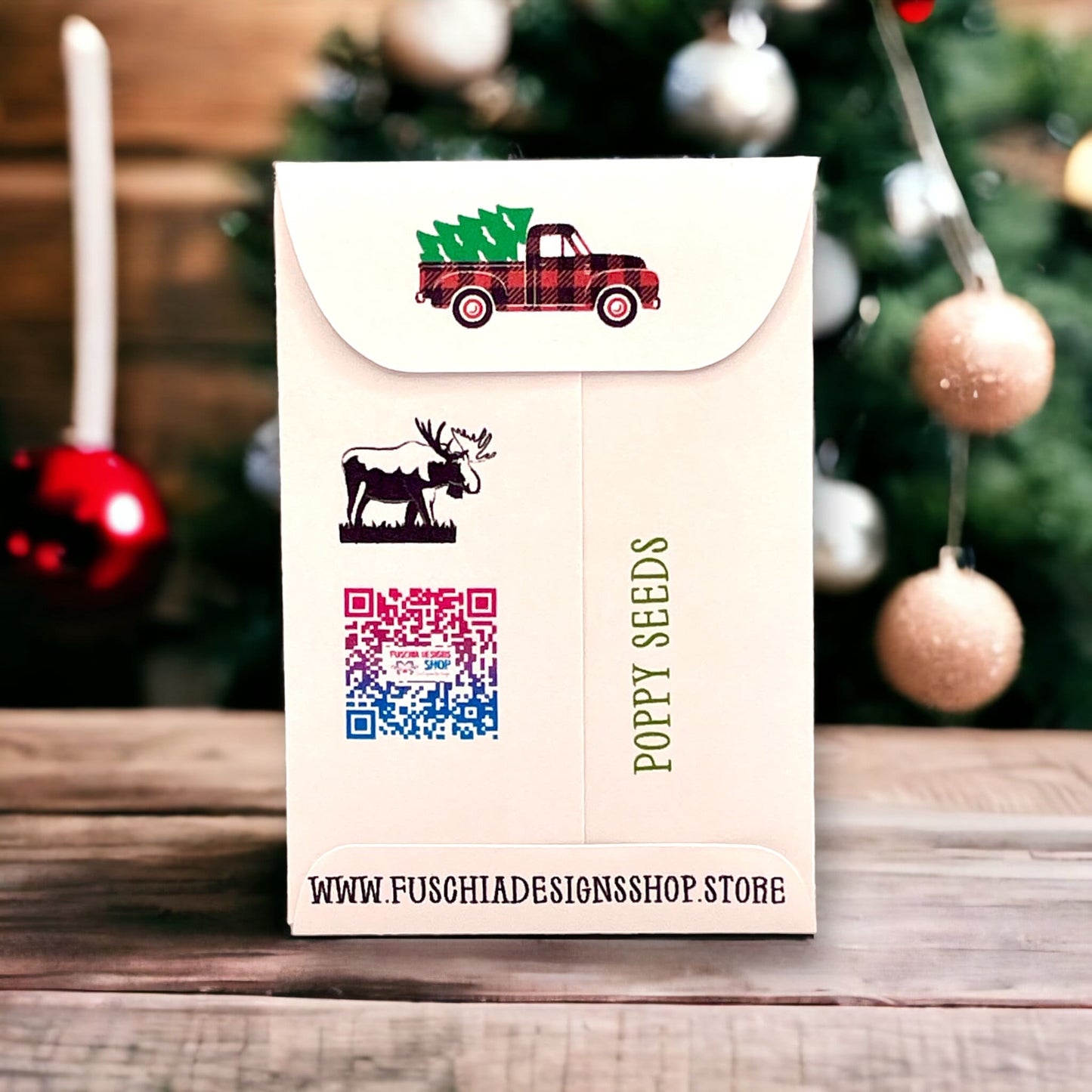 Back of a woodland Christmas seed packet showing a buffalo-plaid truck carrying a Christmas tree on the flap, a moose silhouette, a QR code, 'Poppy Seeds' and the Fuschia Designs Shop website