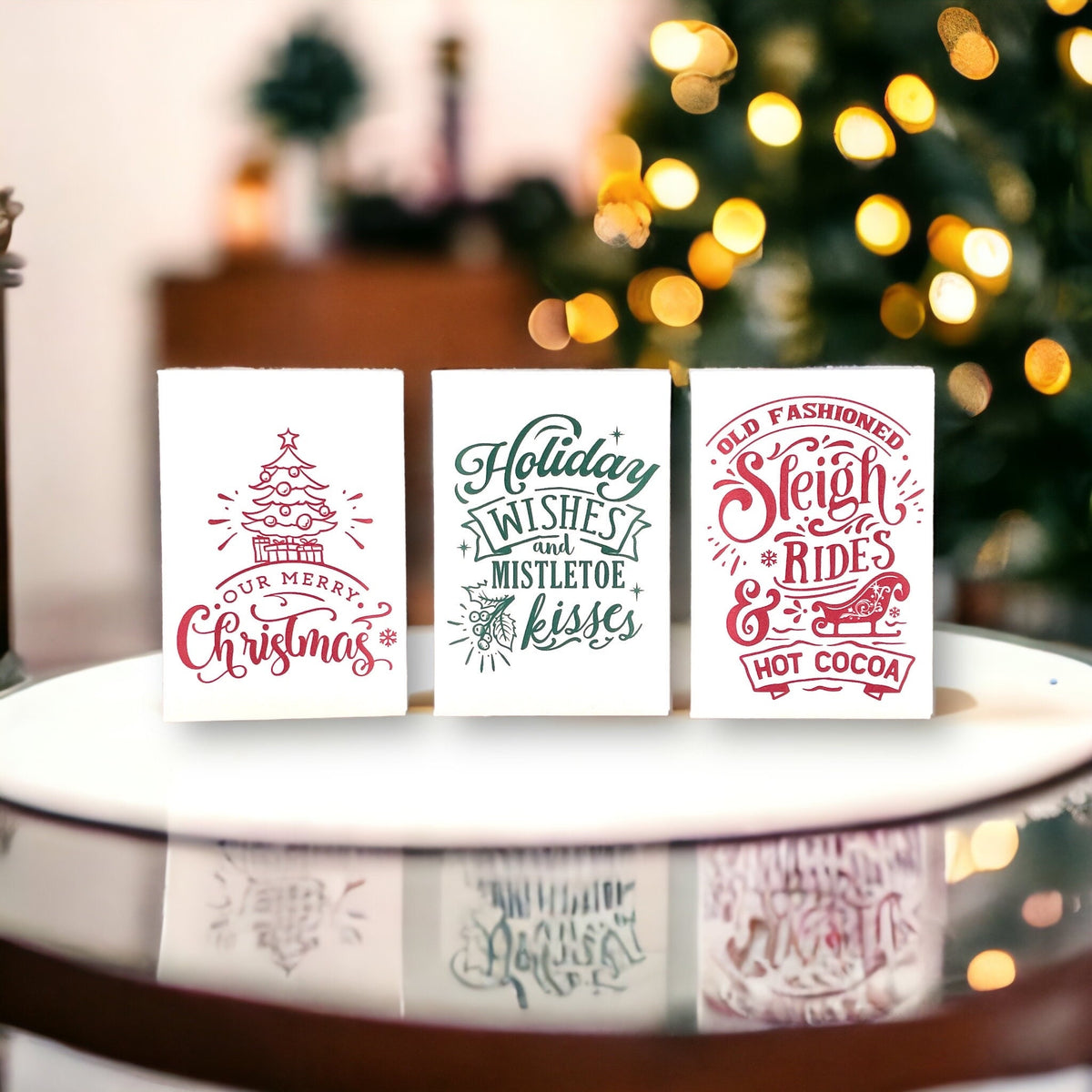Three vintage-style Christmas seed packets on a glass table in front of Christmas tree lights, reading 'Our Merry Christmas', 'Holiday wishes and mistletoe kisses' and 'Old fashioned sleigh rides and hot cocoa'