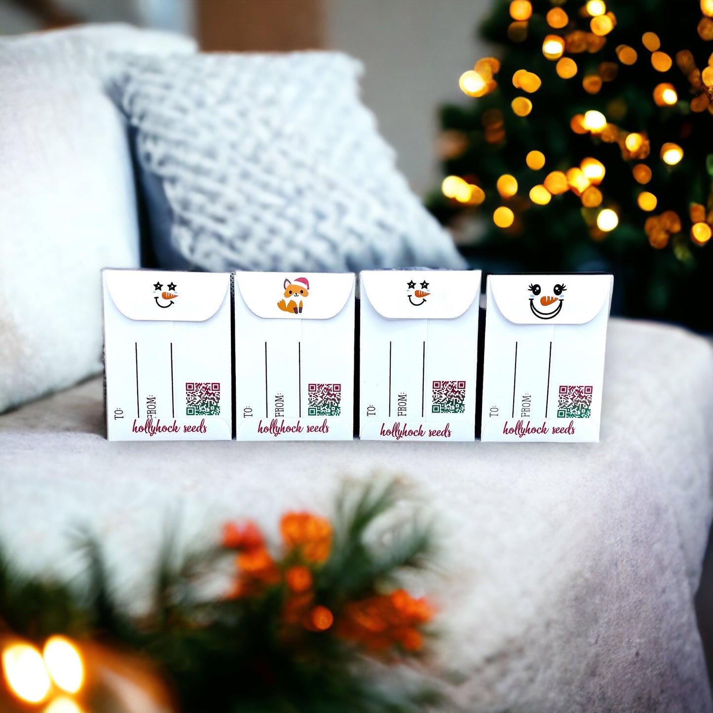 Backs of four Christmas Wish hollyhock seed packets showing To and From lines, QR codes and flap designs of snowman faces and a fox, in front of a lit Christmas tree