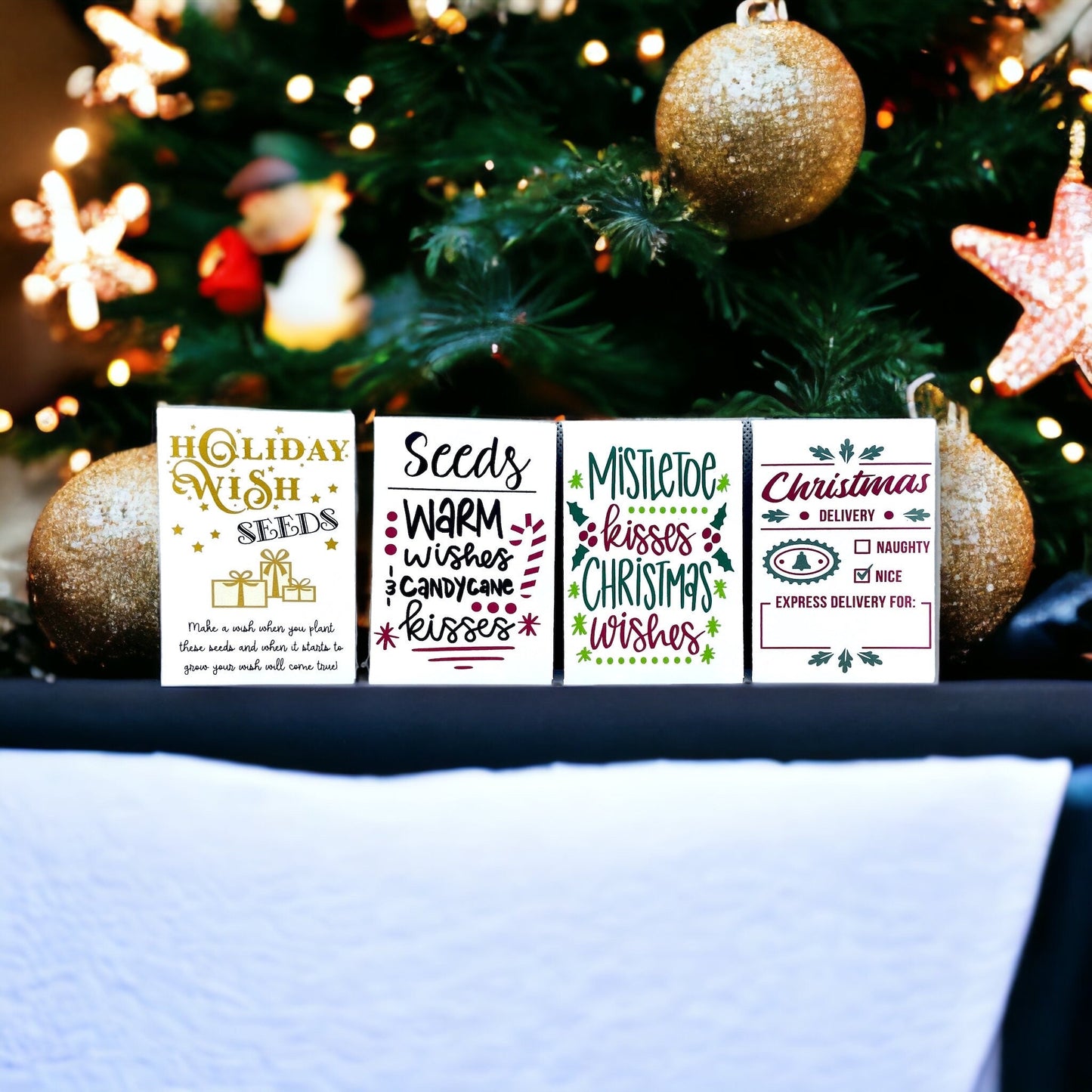 Four Christmas seed packets standing in front of a decorated Christmas tree, reading 'Holiday Wish Seeds', 'Warm wishes and candy cane kisses', 'Mistletoe kisses Christmas wishes' and 'Christmas Delivery' with a naughty or nice checklist