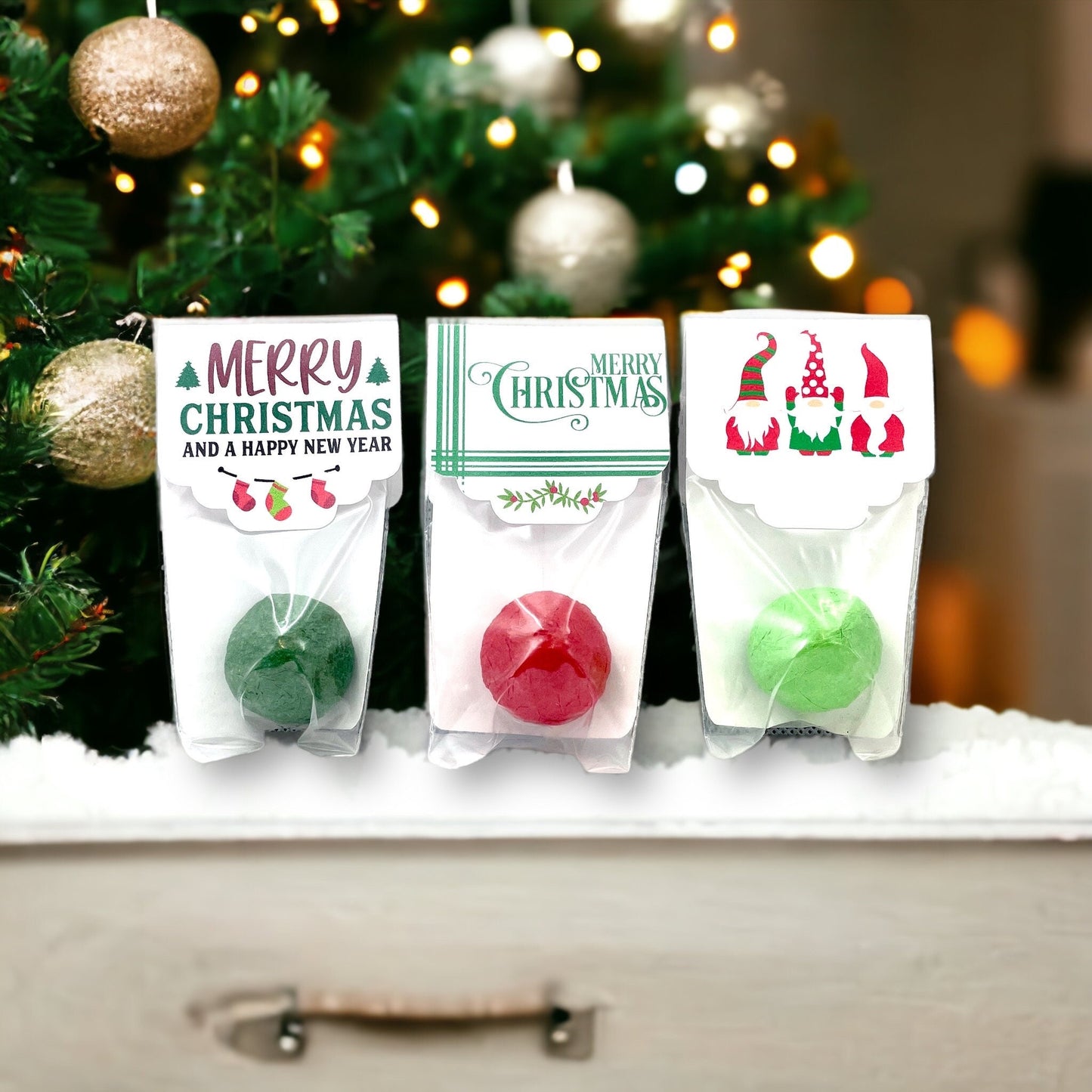 Three individually wrapped Christmas seed bombs in front of a Christmas tree, with toppers reading 'Merry Christmas and a Happy New Year', 'Merry Christmas' and a design of three Christmas gnomes
