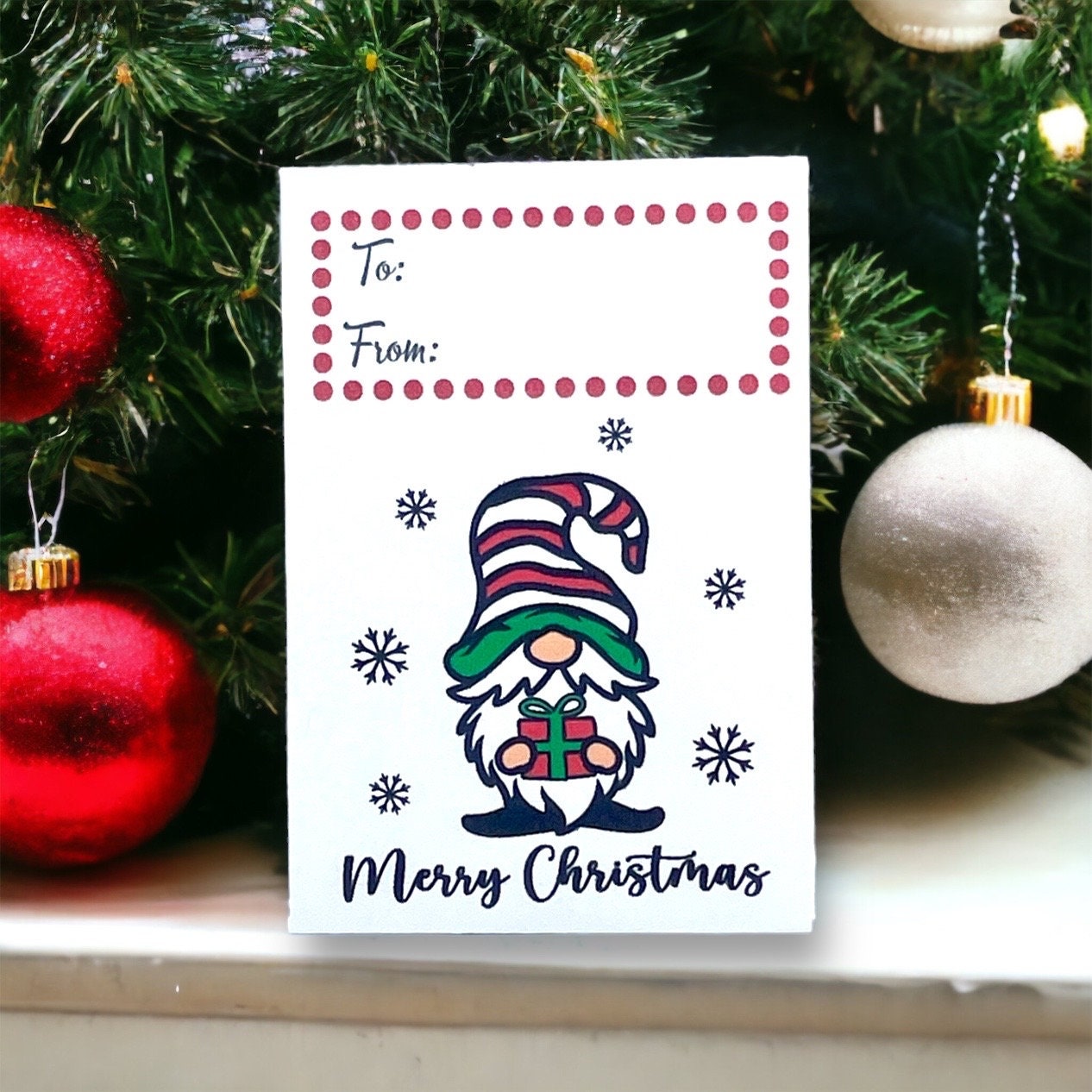 Christmas seed packet with a gnome in a striped hat holding a gift, surrounded by snowflakes above the words 'Merry Christmas', with To and From boxes at the top and red and white baubles beside it